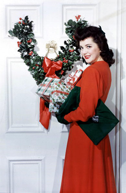 1953. A picture of American film actress Ann Rutherford, standing with Christmas presents next to a door decorated with a holly wreath.