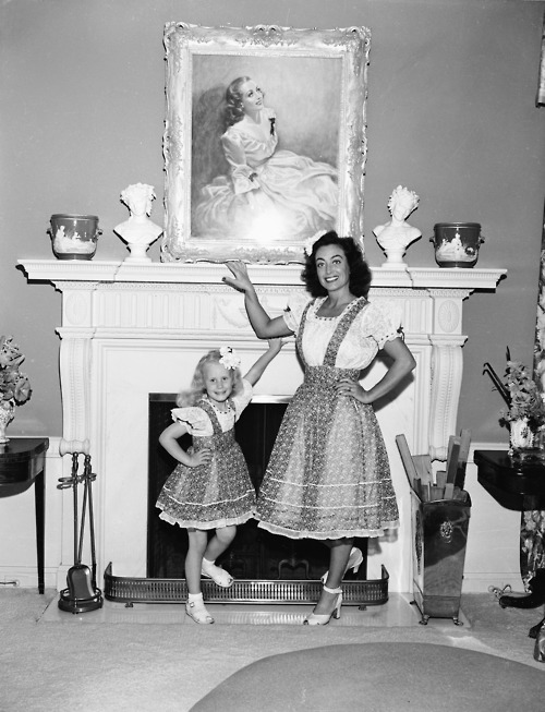 American actor Joan Crawford (1904 - 1977) poses by a fireplace with her adopted daughter Christina, June 1944. (Photo by Gene Lester/Getty Images)