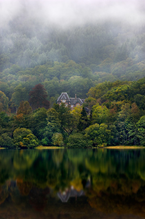 Image taken from the shoreline of the beautiful Loch Achray, Scotland. The low mist slowly drifts along the hillside behind the lovely house nestled in amongst the forest trees on the far shoreline. A longer exposure was used to smooth ripples from the water and produce a beautiful reflection.