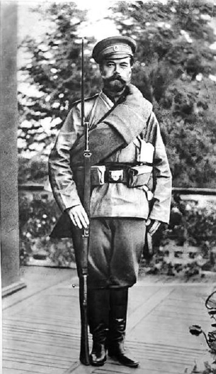 Keisari Nikolai II tavallisen sotilaan univormussa suoraan edestä päin kuvattuna rakennuksen kuistilla. Taustalla puiden lehvästöä. Kuvatekstit alapuolella painettuna kyrillisin kirjaimin.