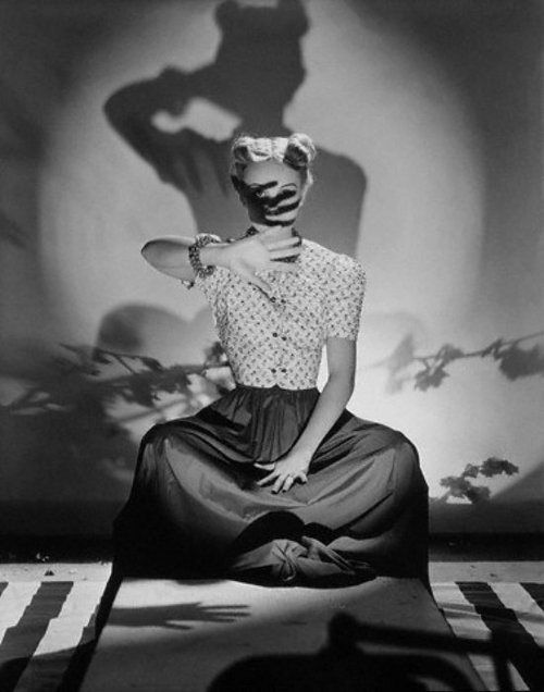 ca. 1938 --- Model, Bunny Hartley, wearing short-sleeved, form-fitting quilted jacket with flower print, dark skirt, and matching necklace and bracelet, seated with her hand shielding her face. --- Image by © Condé Nast Archive/Corbis